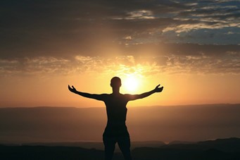 Homme face au coucher de soleil à bras ouverts